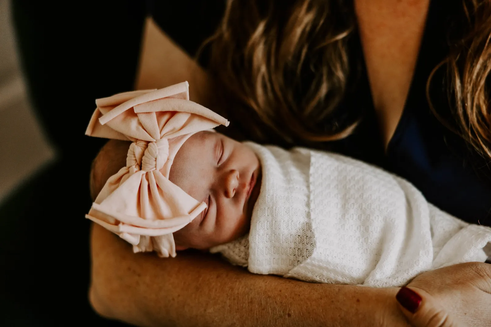 Newborn in a large pink bow asleep on her mother's arm