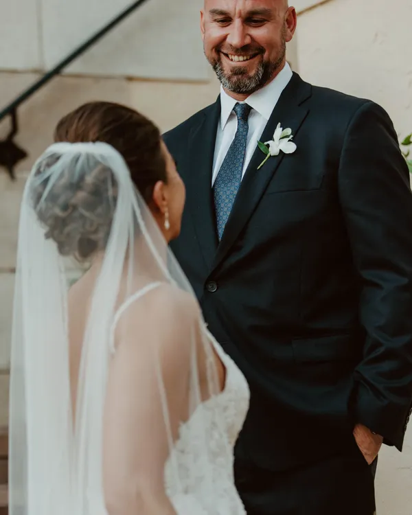Groom smiling down at his bride, seen over her veiled shoulder