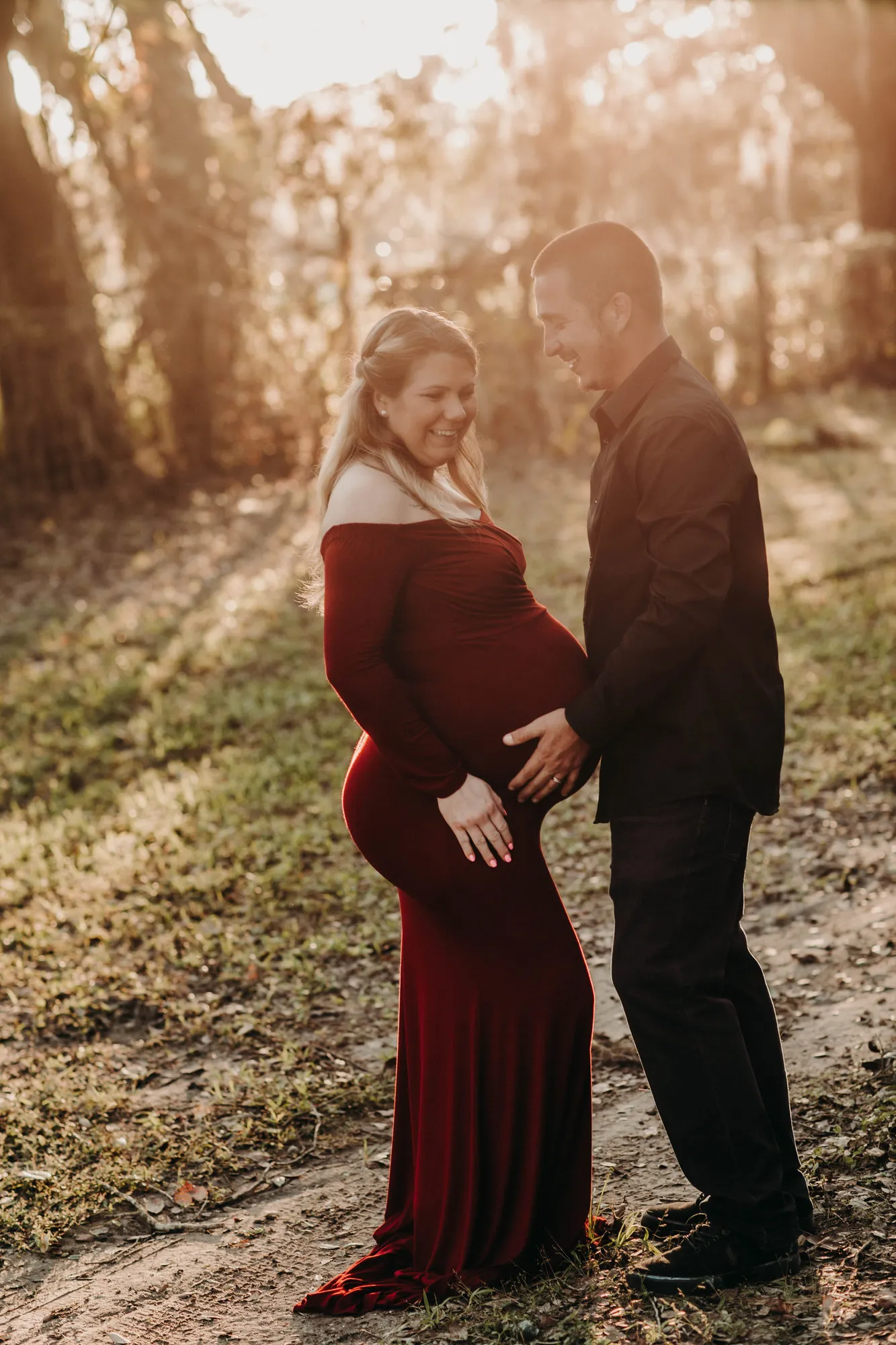 Expectant couple facing each other in golden backlight, her hands on her bump
