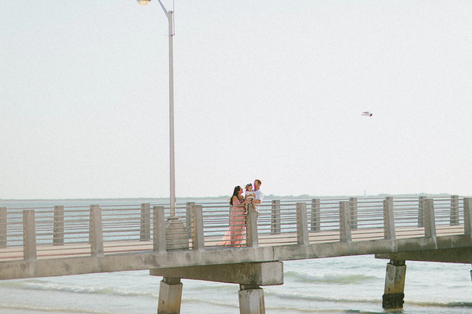 Family of three on the pier, small against a pale sky