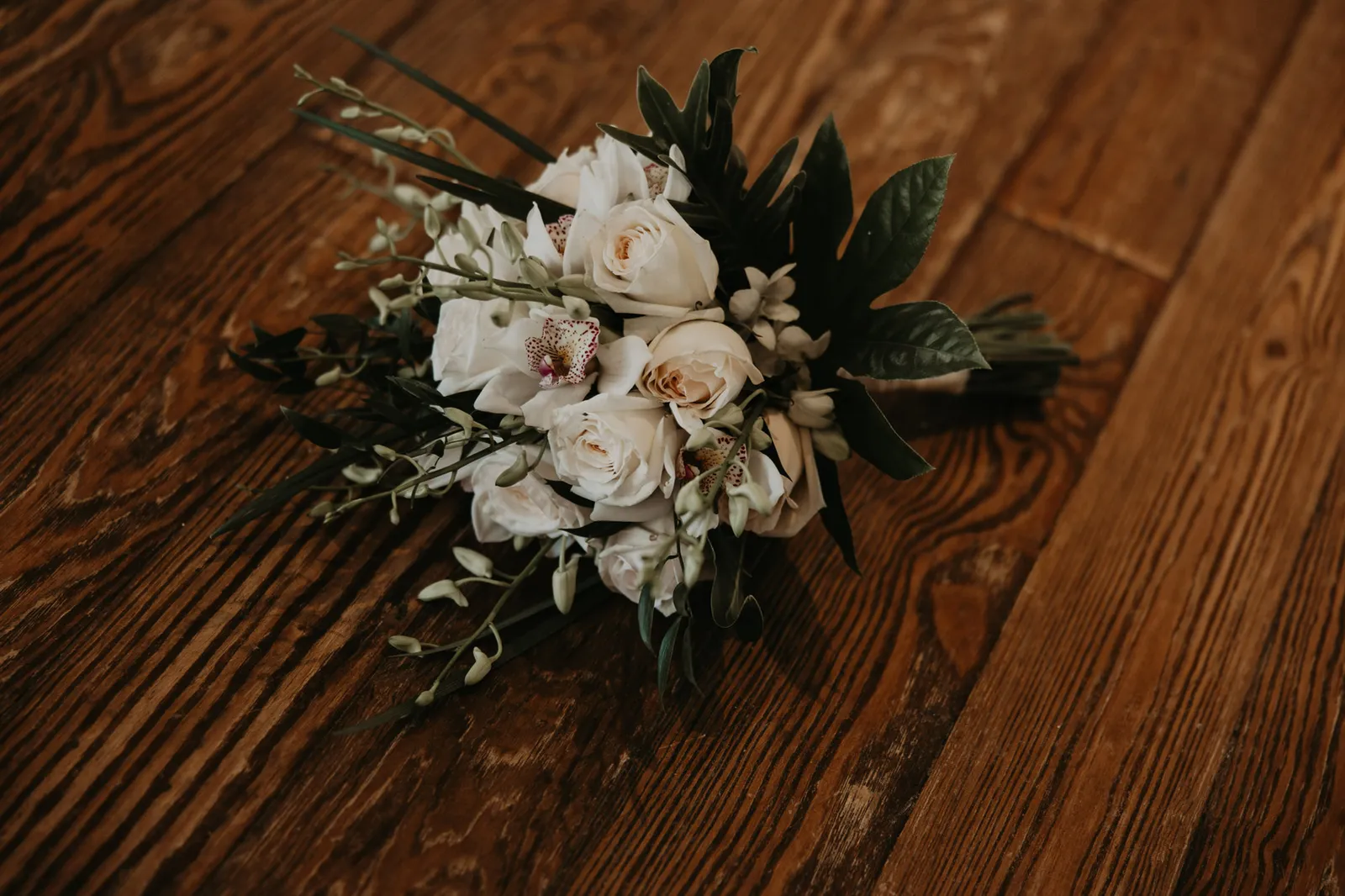 Bouquet of white roses and orchids lying on a wooden floor