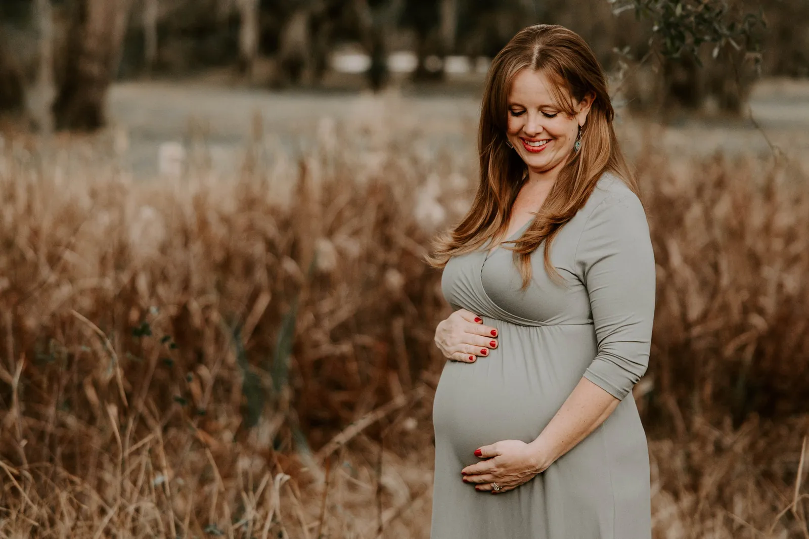 Expectant mother in a sage dress standing in tall grass