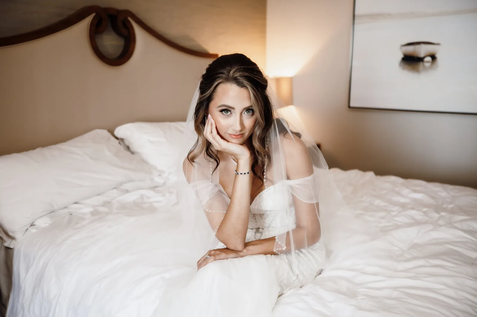Bride in her veil lying on the hotel bed, resting her chin on her hand