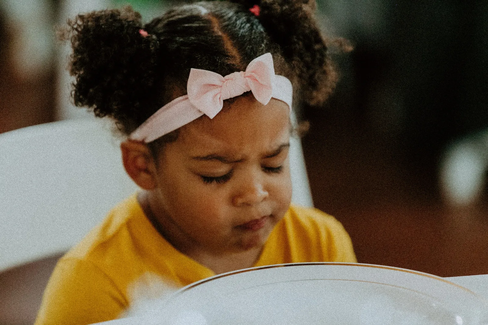Small girl with a pink bow headband frowning in concentration at the table