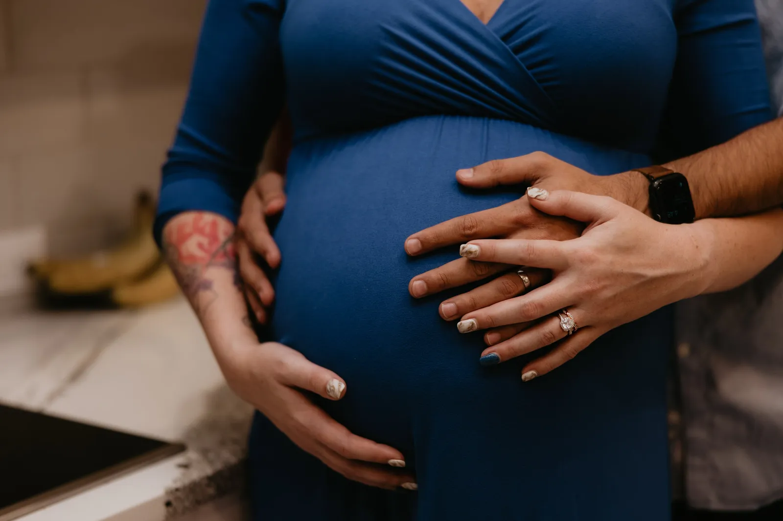 Close-up of the couple's hands on her bump, in the kitchen