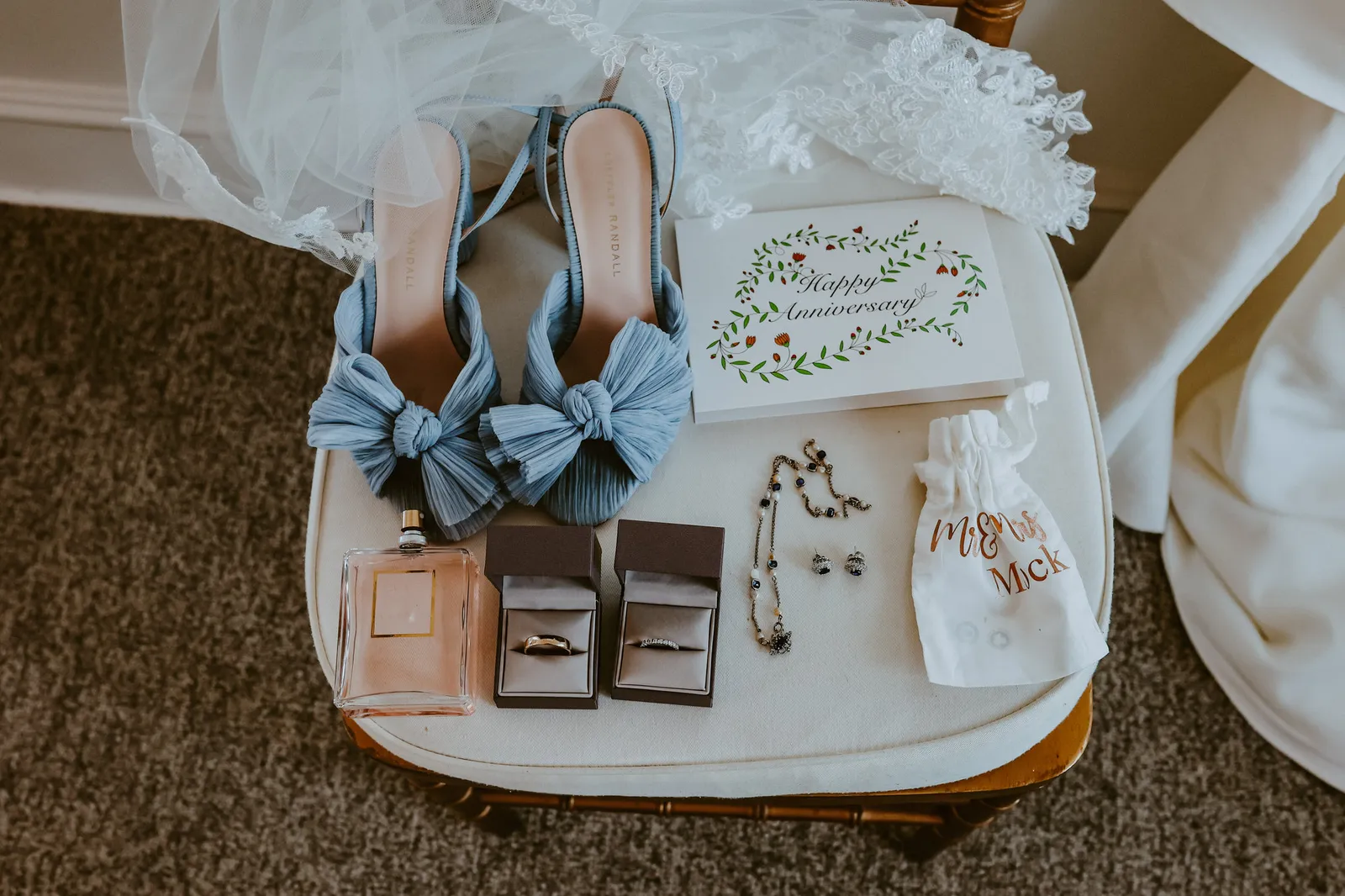 Blue bow wedding shoes laid out on a chair with rings and a vow book