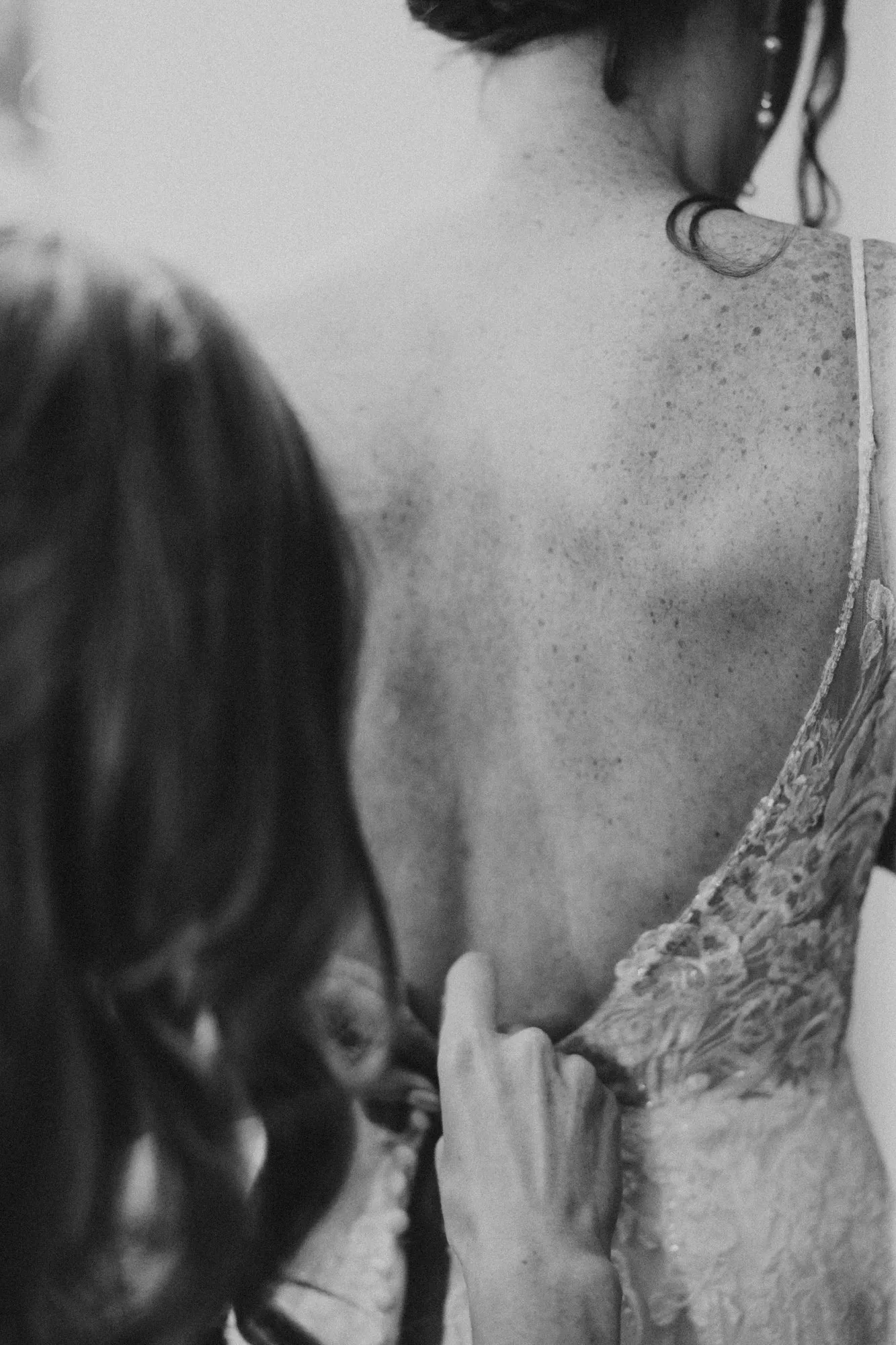 Hands fastening the back of the bride's lace dress, in black and white