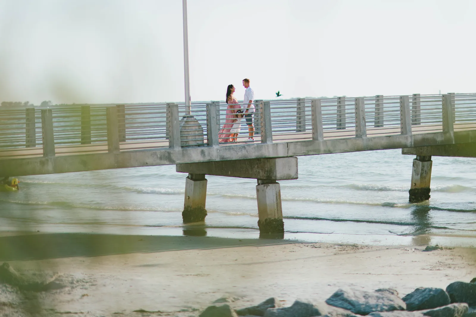 Family standing on the pier above the beach, seen from the shore