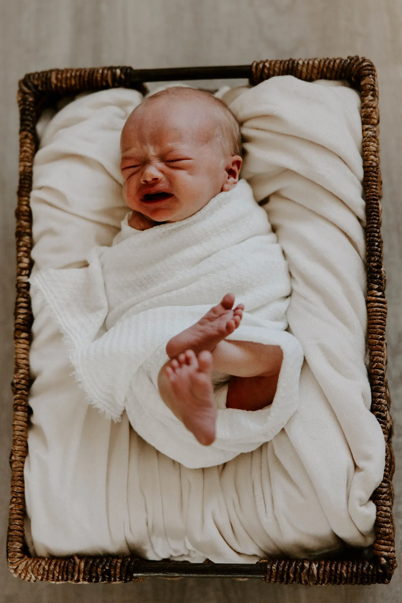 Swaddled newborn crying in a wicker basket, seen from above