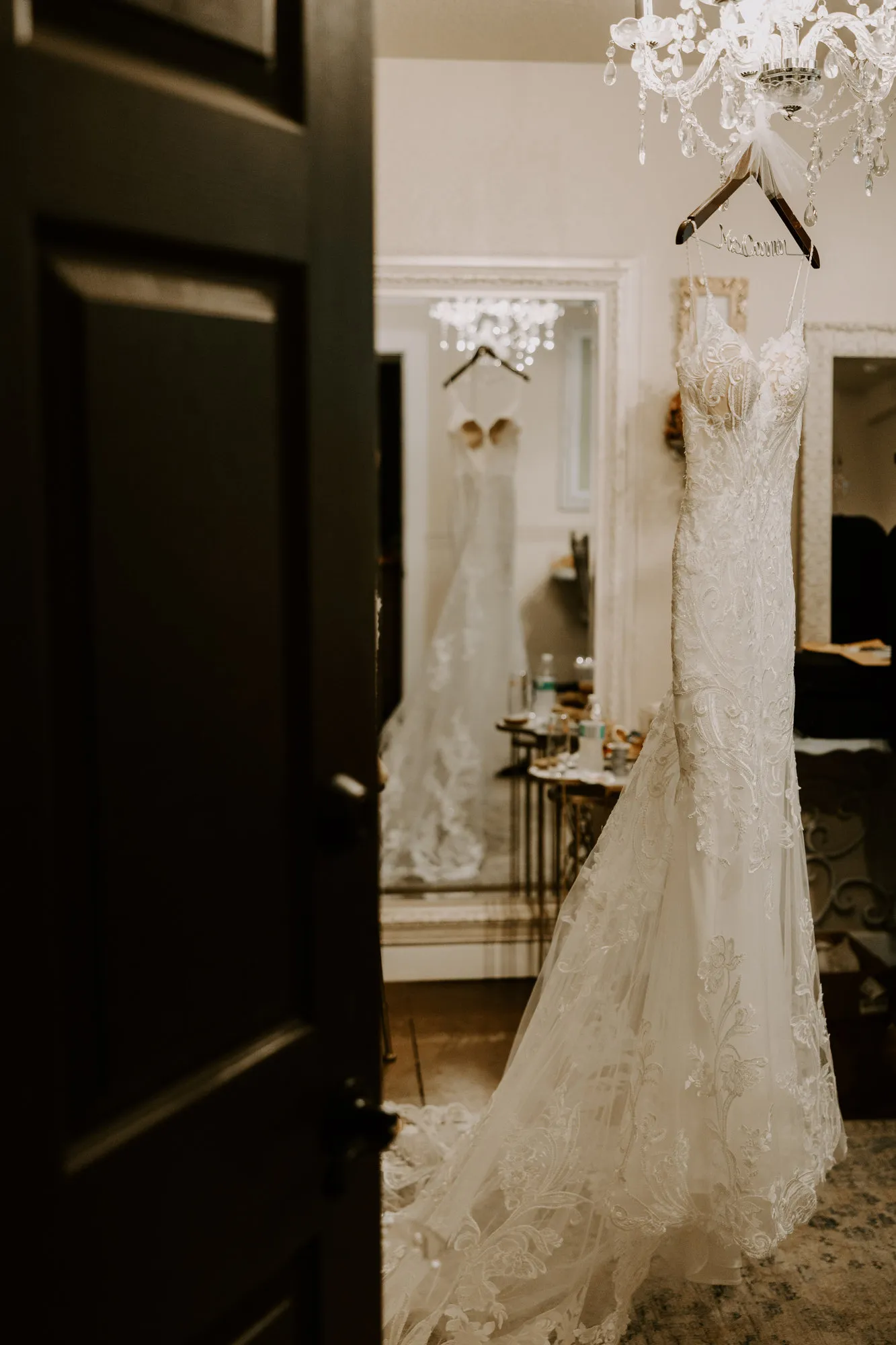 Lace wedding dress hanging in a doorway beneath a chandelier