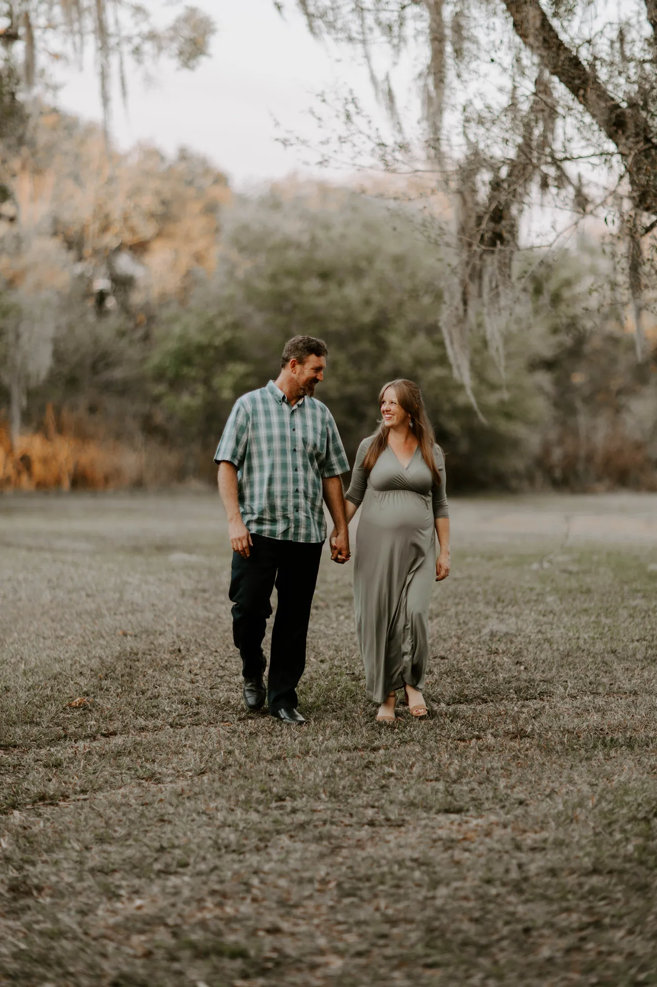 Couple walking hand in hand across a clearing under mossy trees