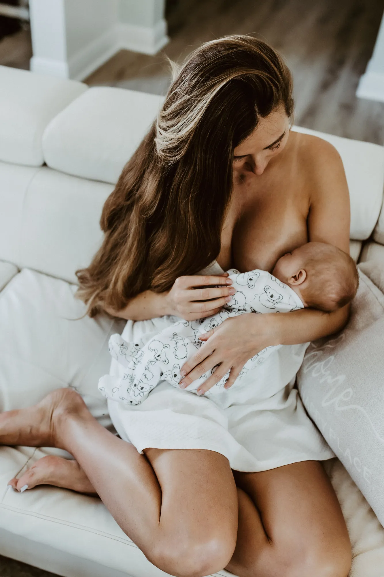 Mother nursing her newborn on a white sofa, seen from above