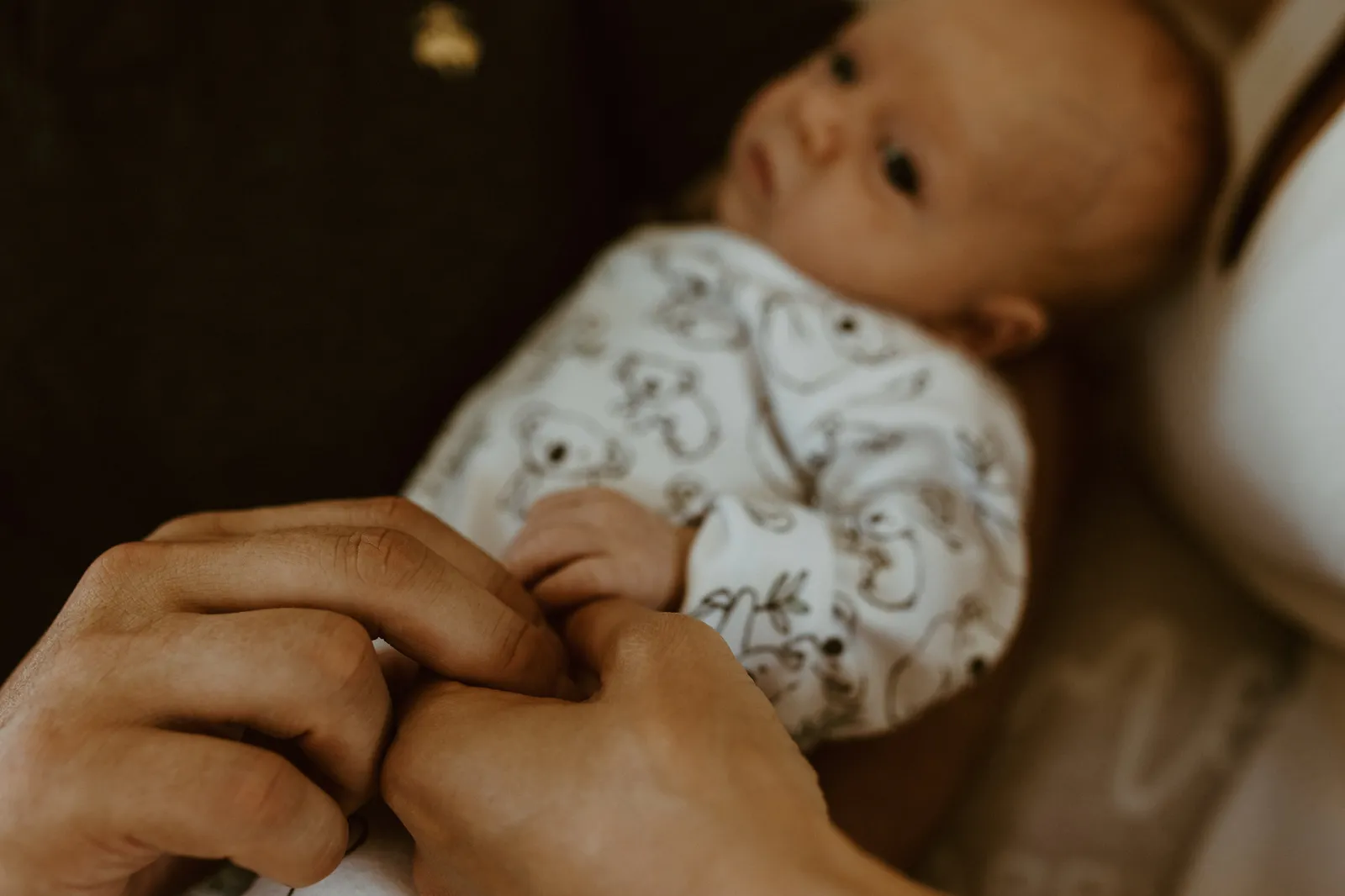Newborn in a koala-print sleepsuit gripping his parent's finger