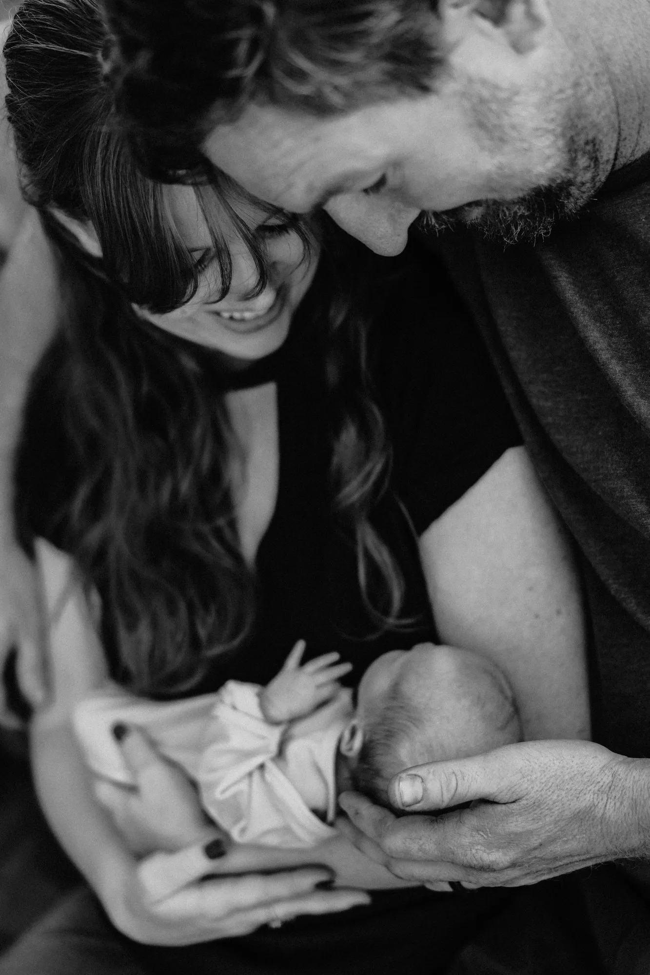 Parents bending over their newborn daughter, in black and white