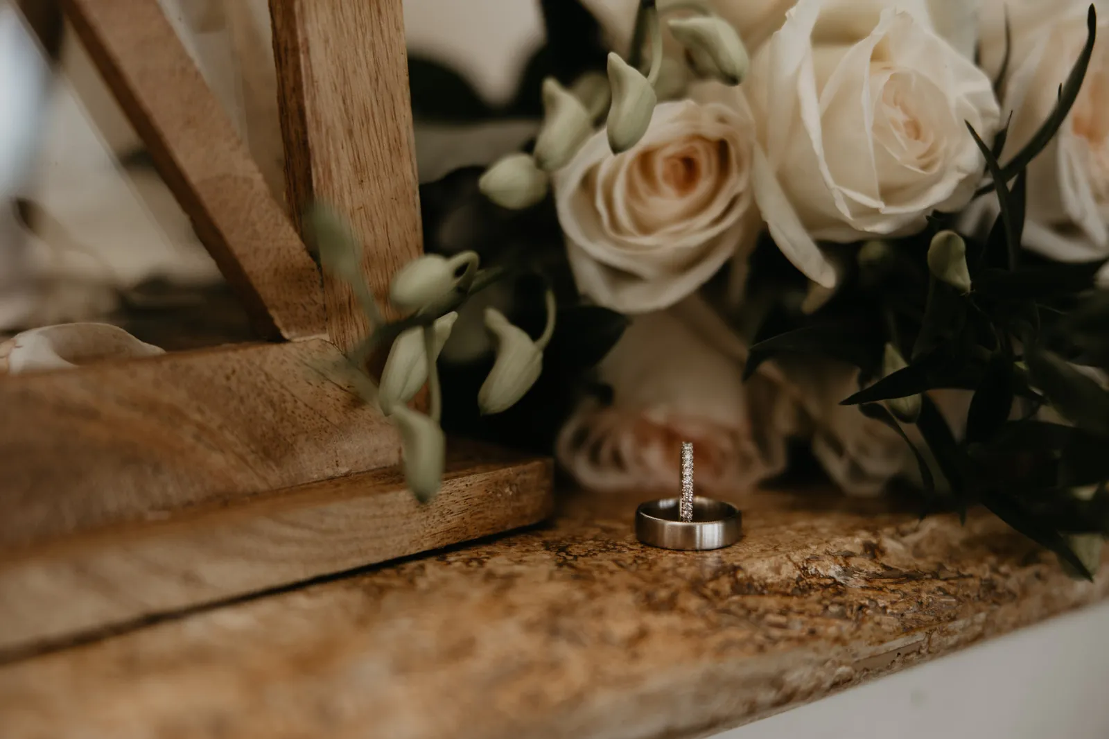 Wedding band tucked beside white roses on a wooden ledge