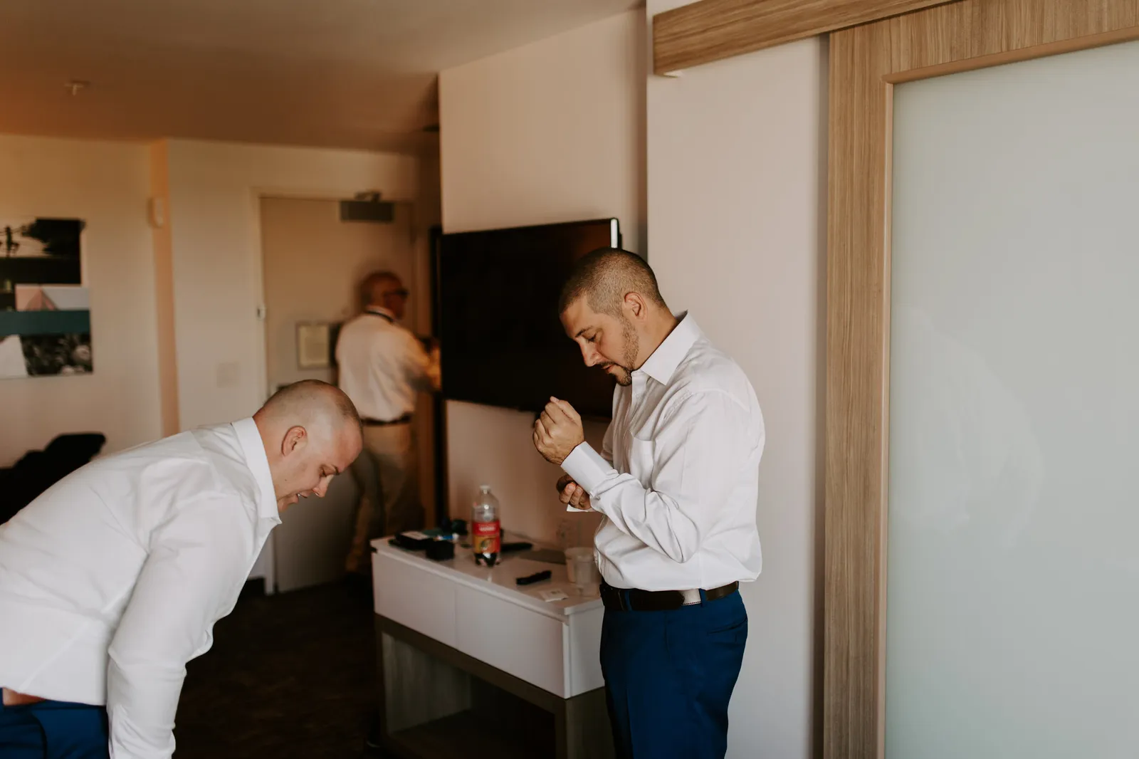 Men in white shirts getting ready in a hotel room, one fastening his cuff