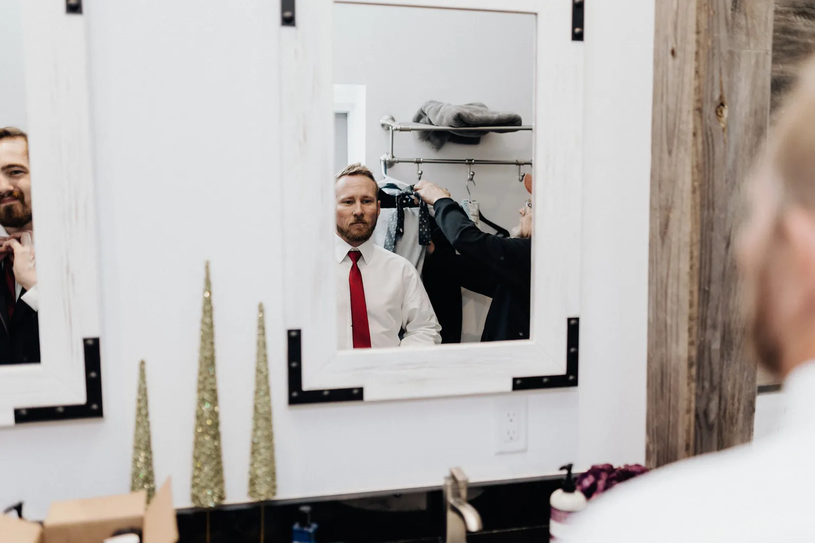 Groom in a red tie reflected in a mirror while he gets dressed