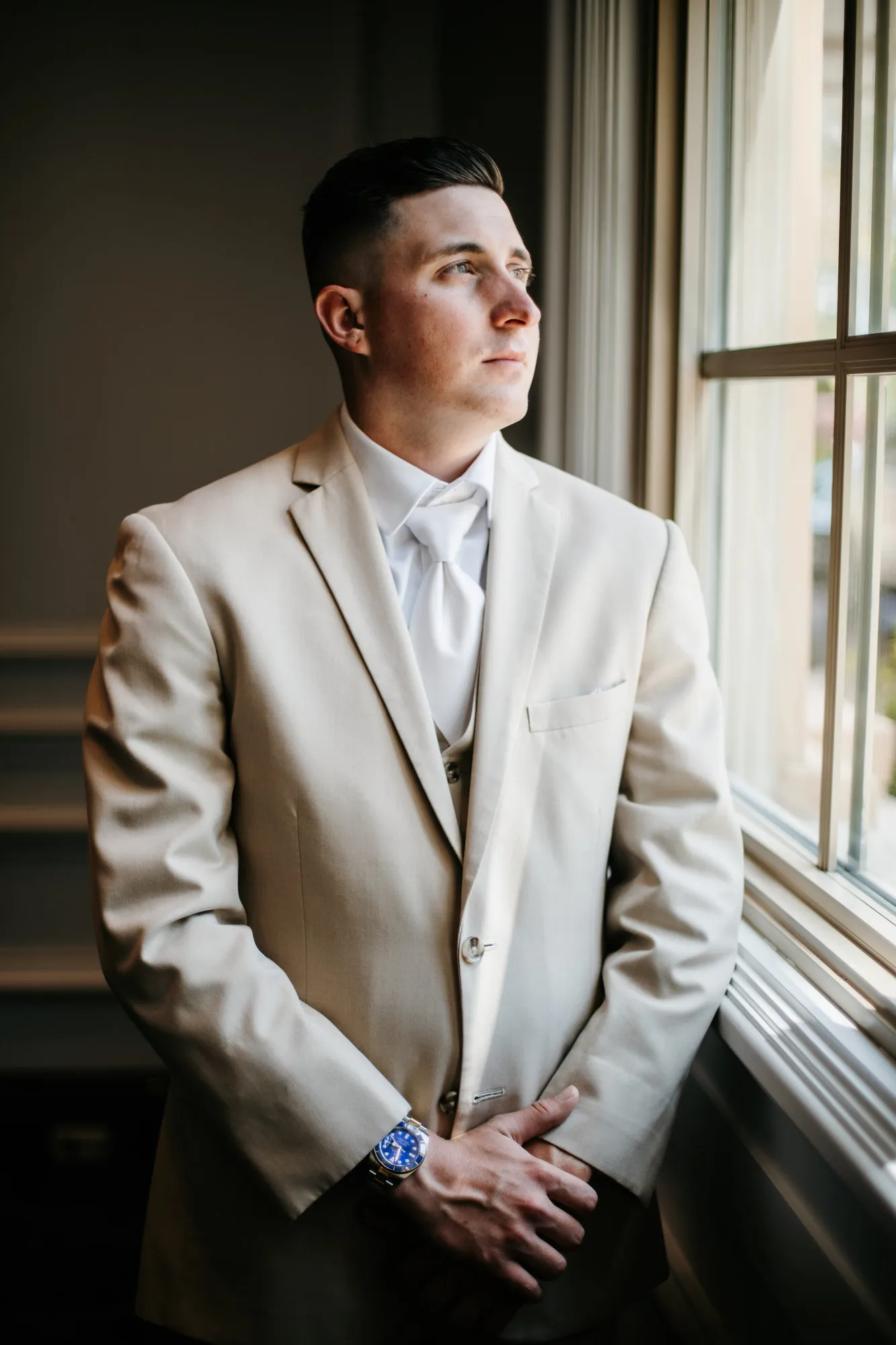 Groom in a tan suit looking out of a window