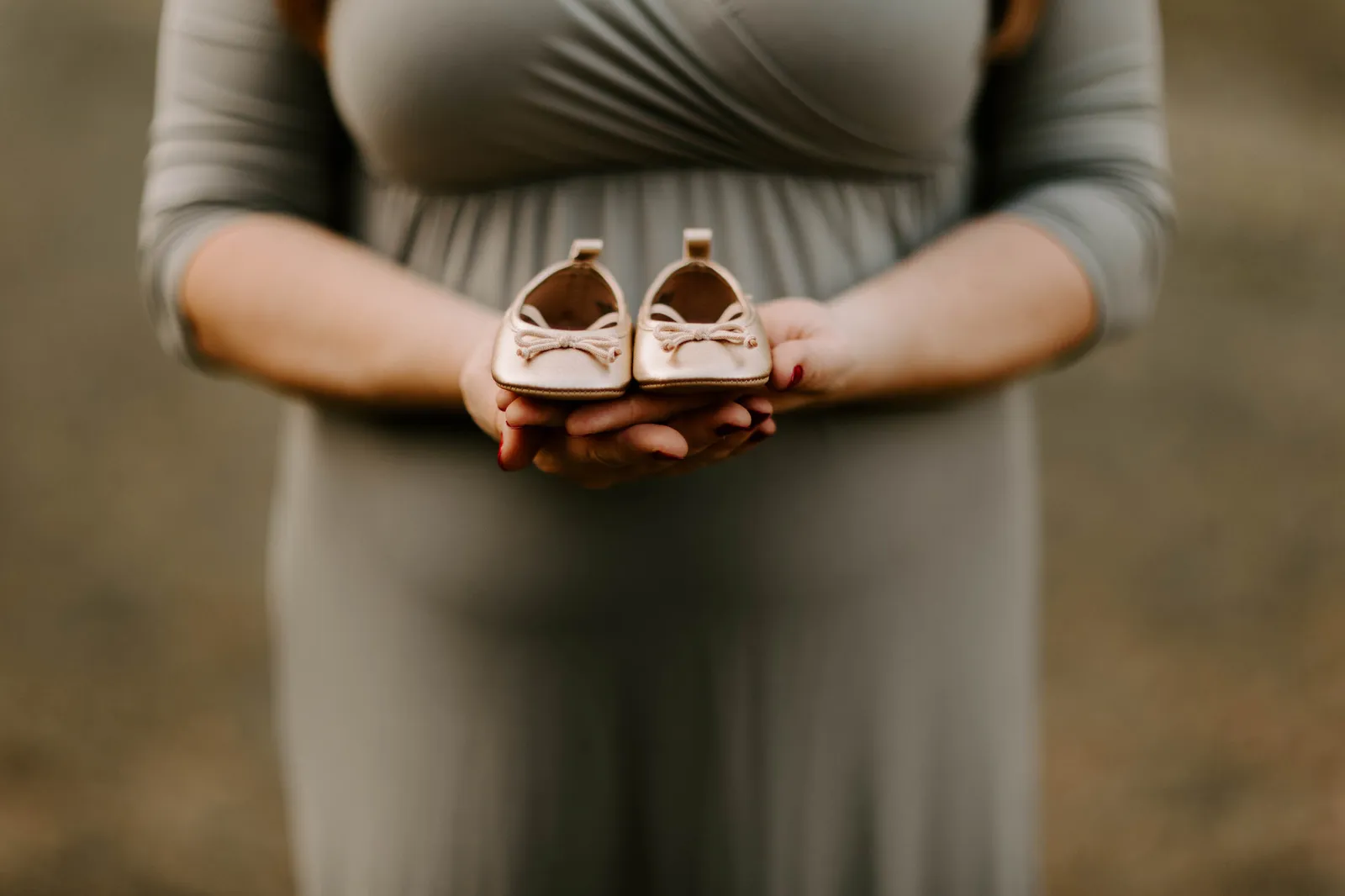Hands holding a tiny pair of baby shoes against her bump