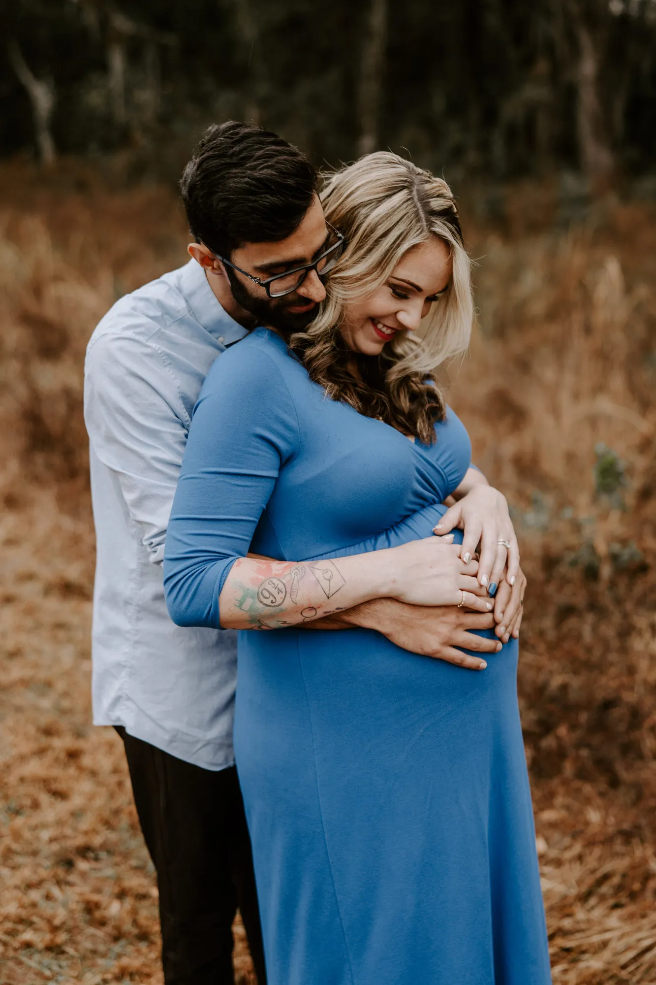 Father-to-be embracing his partner from behind, both hands on her bump