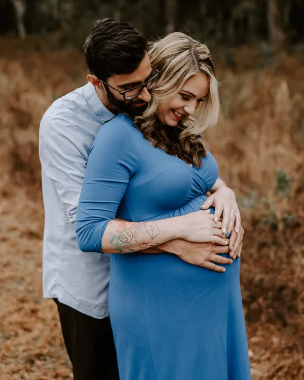 Father-to-be embracing his partner from behind, both hands on her bump