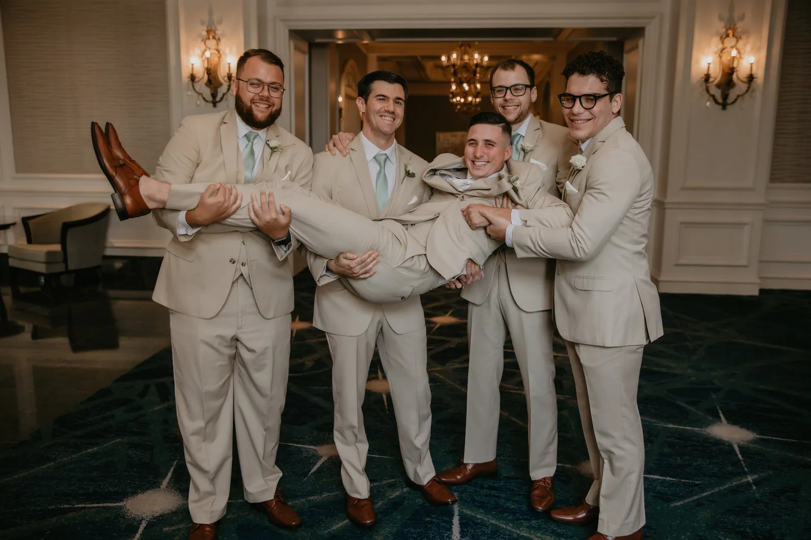 Groomsmen in tan suits lifting the groom off his feet
