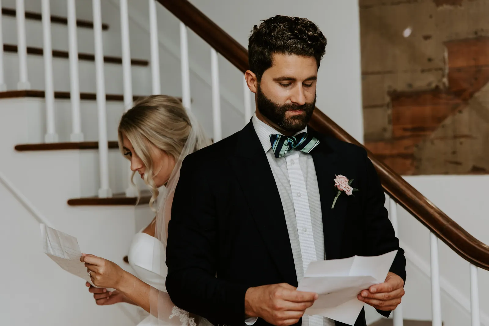 Bride and groom reading letters on either side of a staircase before the ceremony