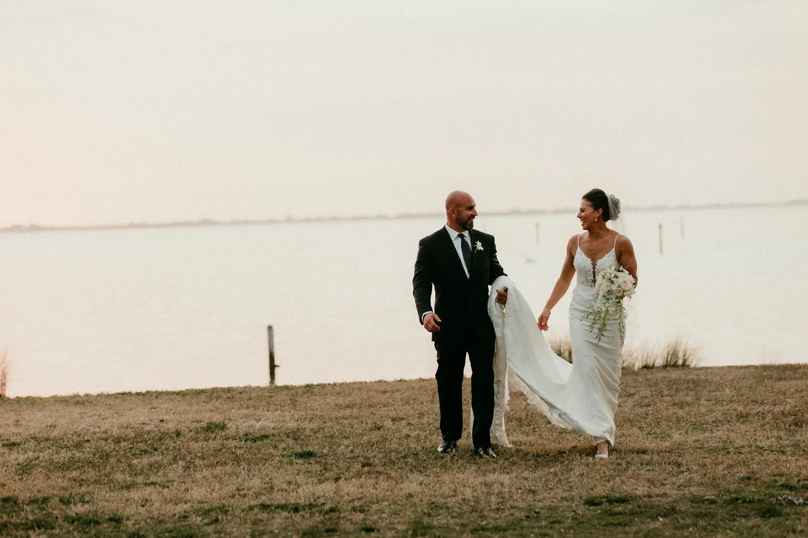 Bride and groom walking along the bayfront lawn at Powel Crosley Estate at dusk