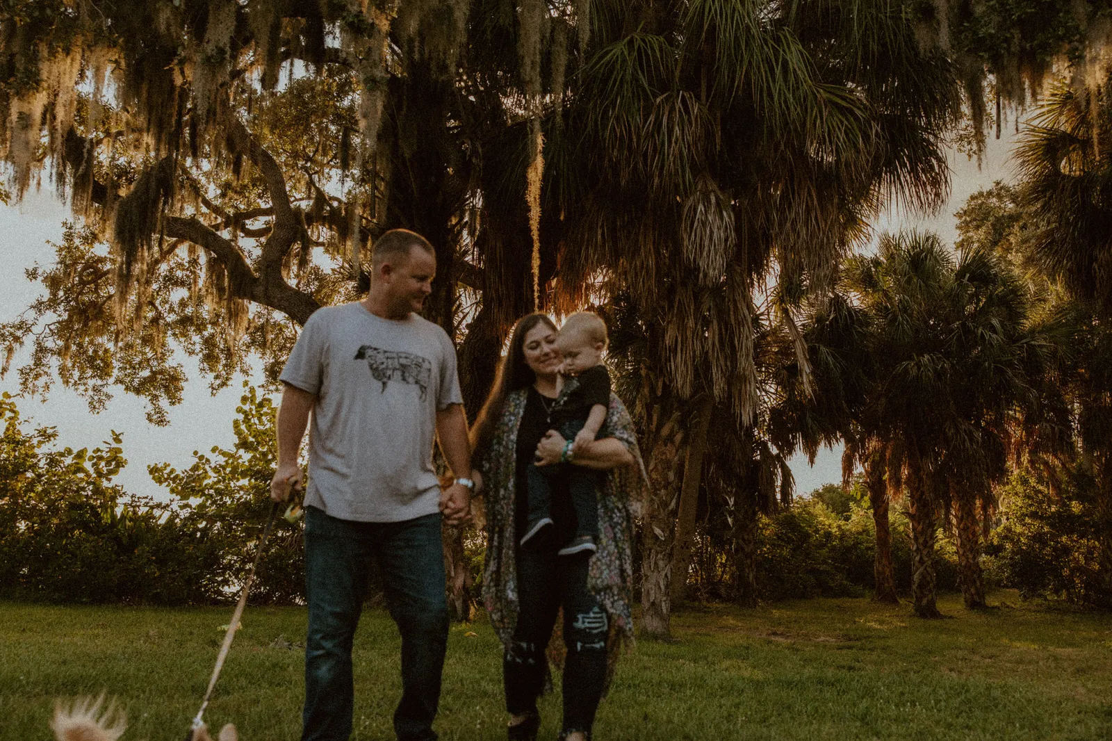 Parents walking hand in hand under a moss-draped oak, the mother carrying their son