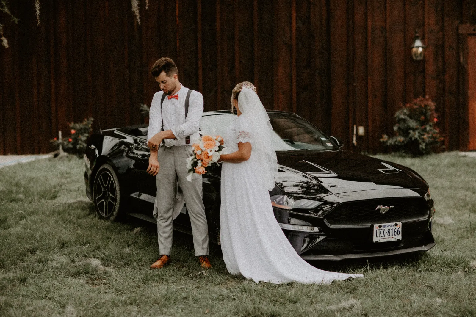 Groom and bride standing back to back beside a black convertible