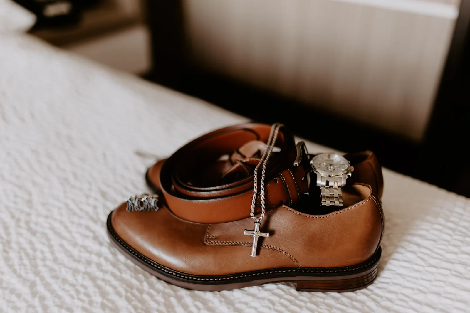 Cross necklace and wedding rings arranged on a brown leather shoe