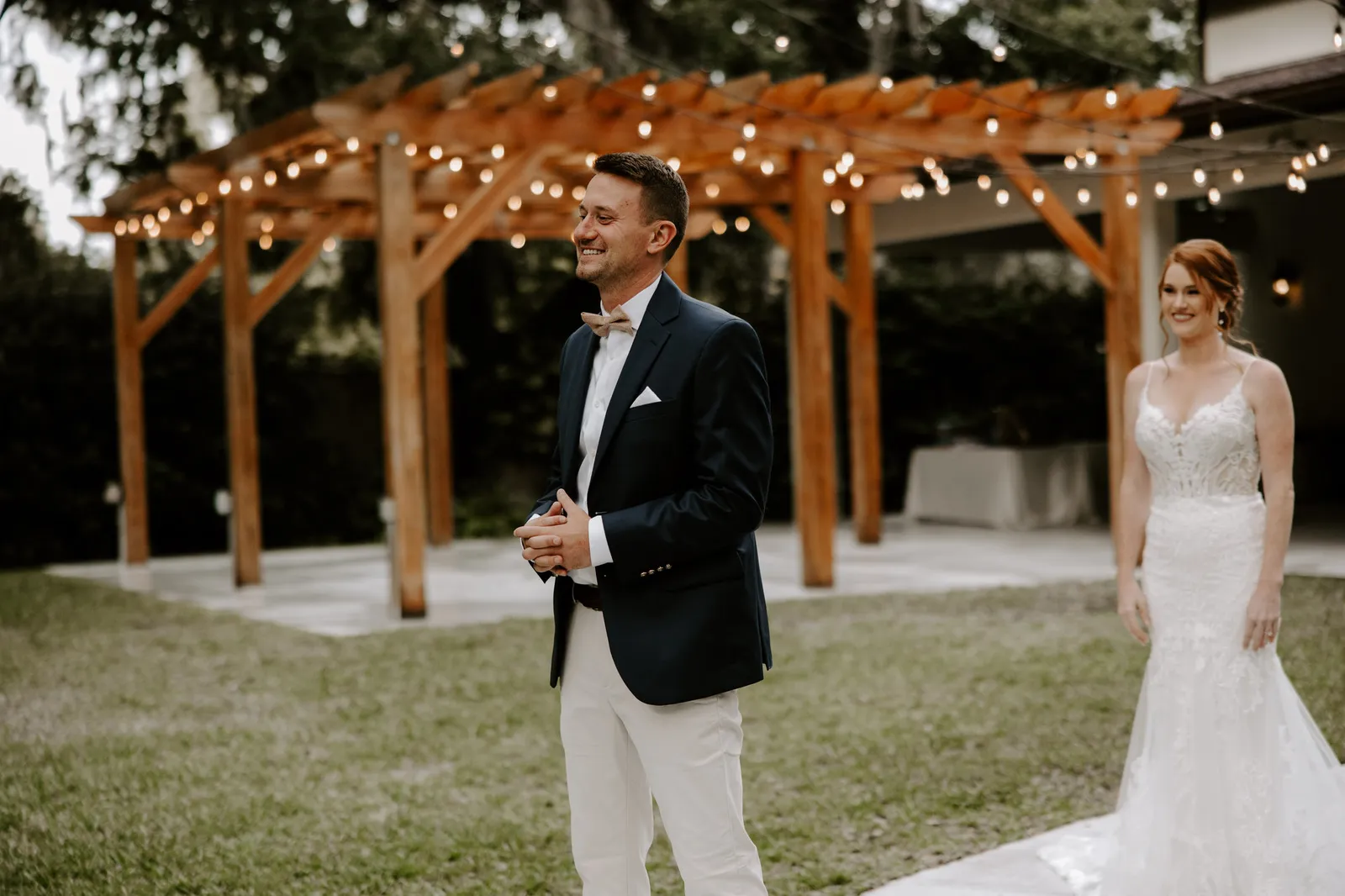 Groom laughing with his back turned as the bride walks up behind him for their first look