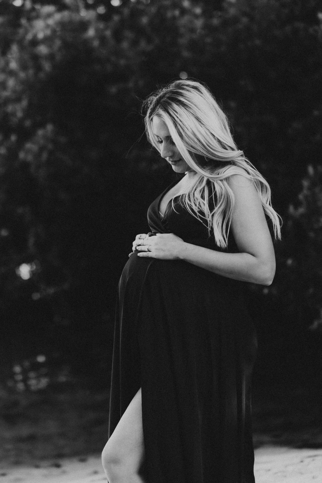 Expectant mother in a dark gown looking down at her bump, in black and white