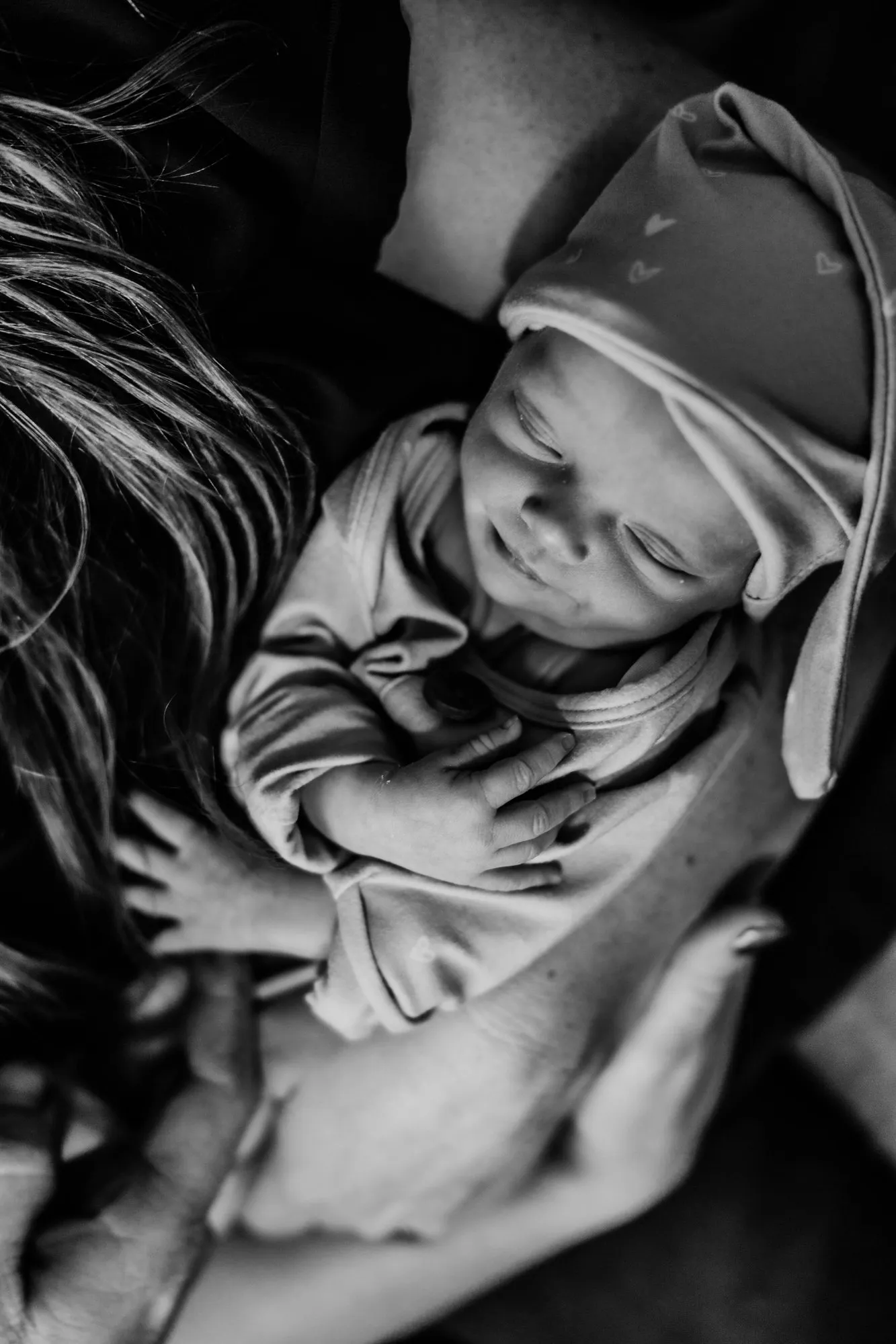 Newborn in a sleep cap resting on her mother's chest, in black and white