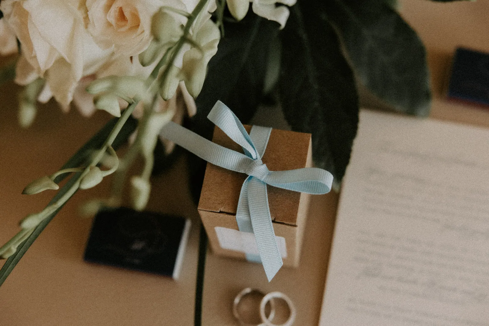 Wedding rings beside a gift box tied with blue ribbon and a handwritten card