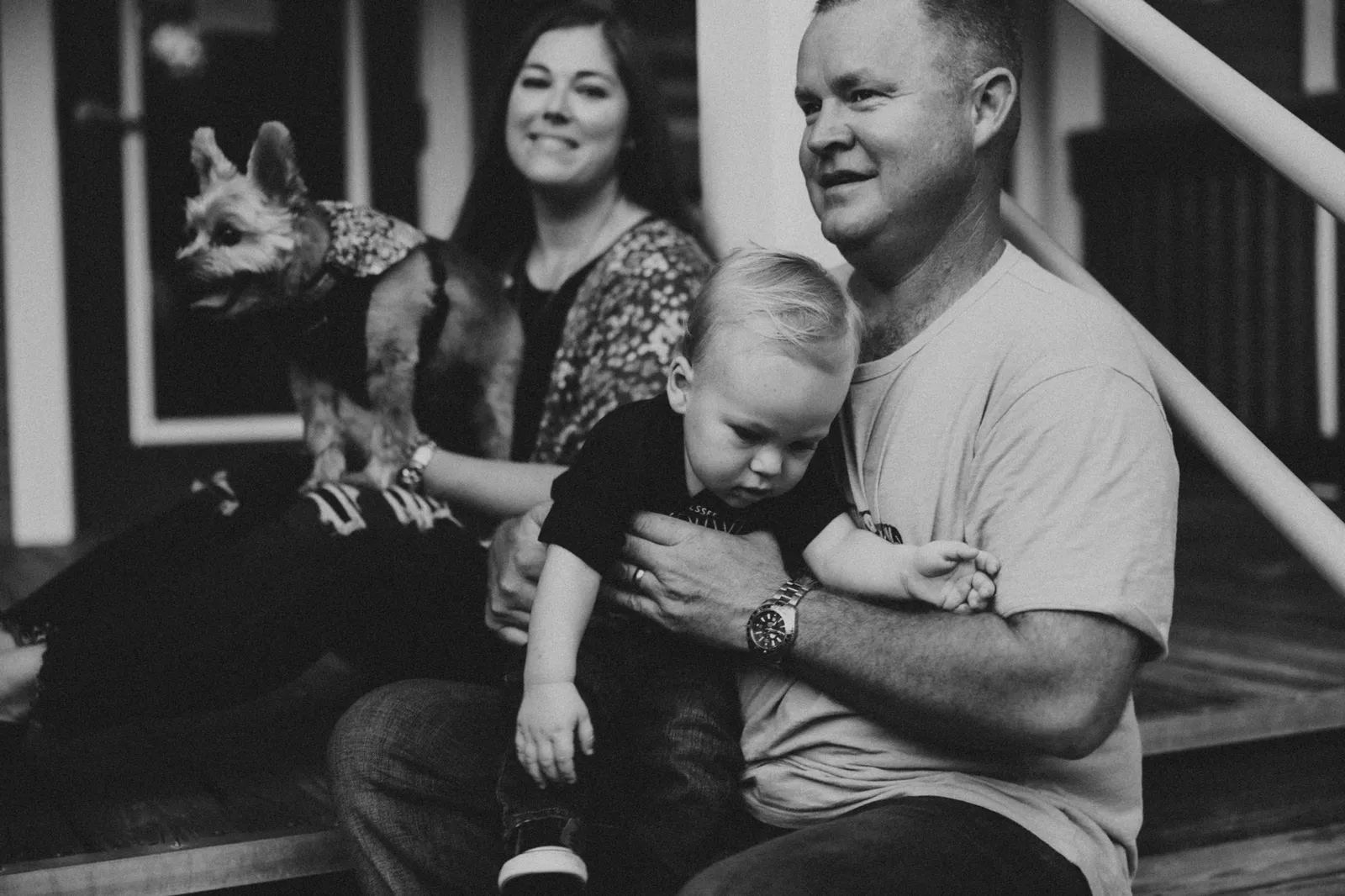Family sitting on porch steps with their small dog, in black and white