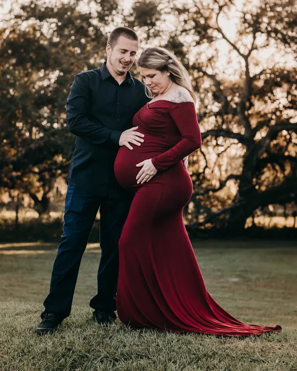 Expectant couple in front of a sprawling oak, she in a long red dress