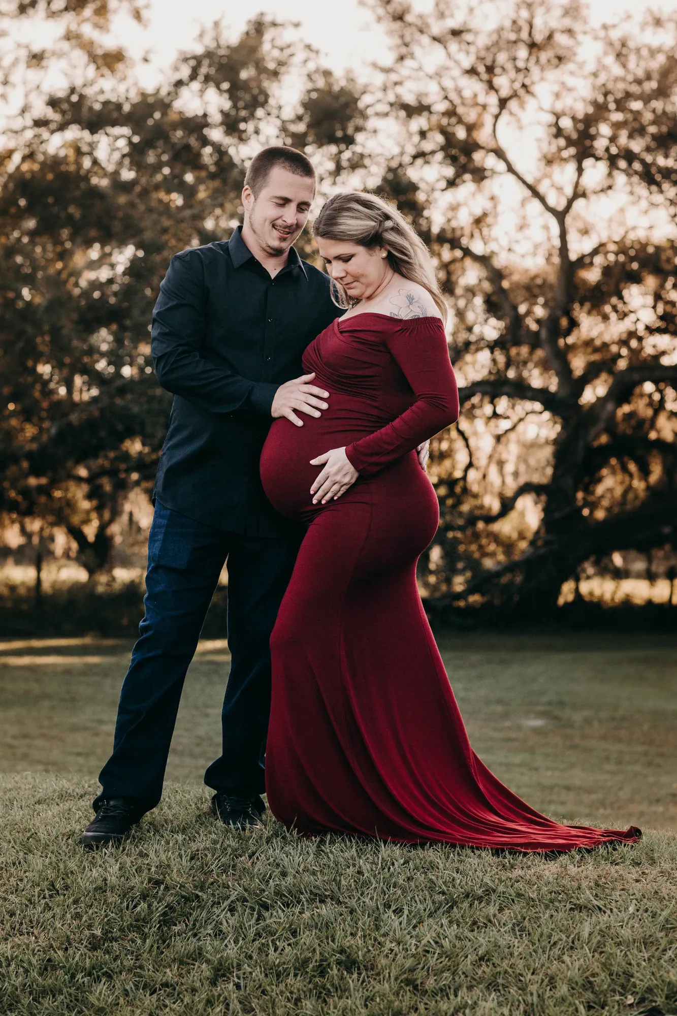 Expectant couple in front of a sprawling oak, she in a long red dress