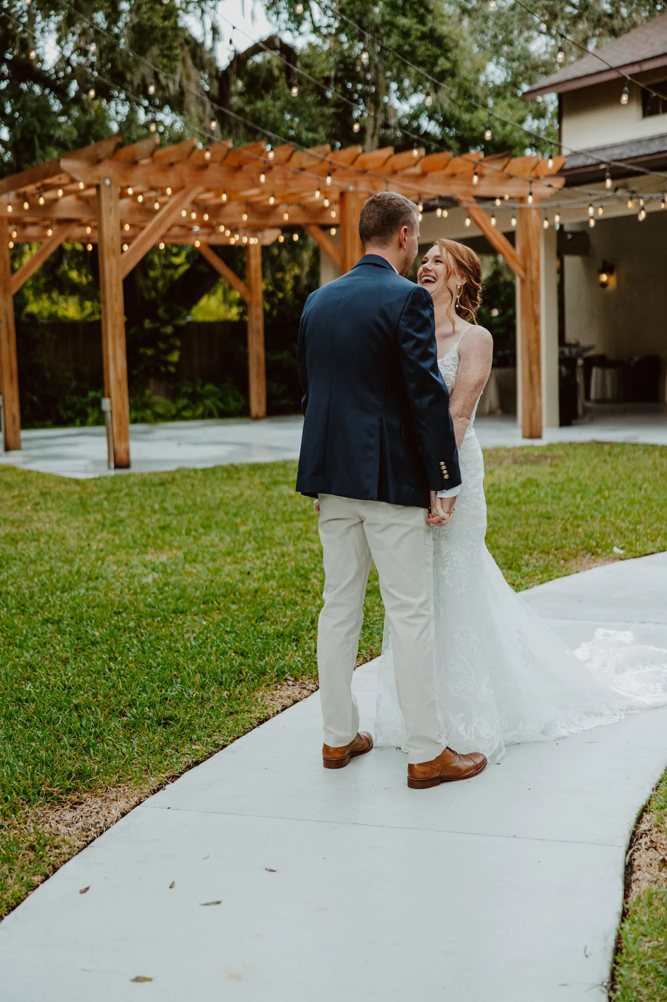 Bride laughing with the groom on the path beside the pergola