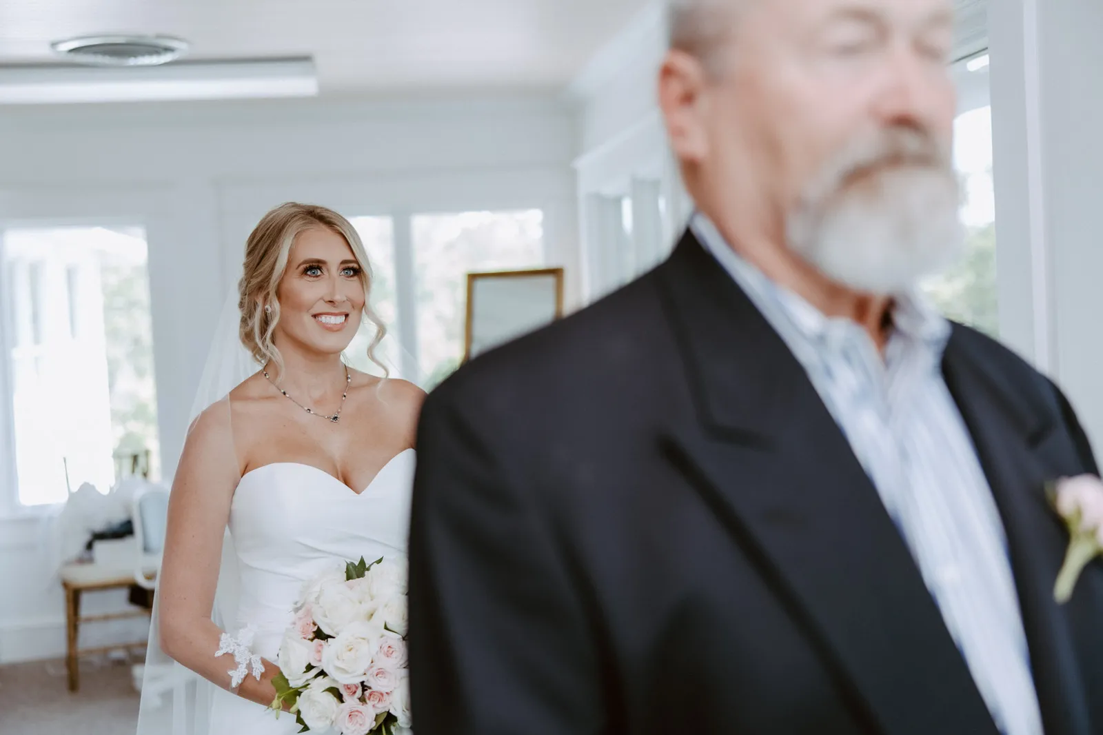 Bride smiling behind a man in a dark jacket who has his back to her