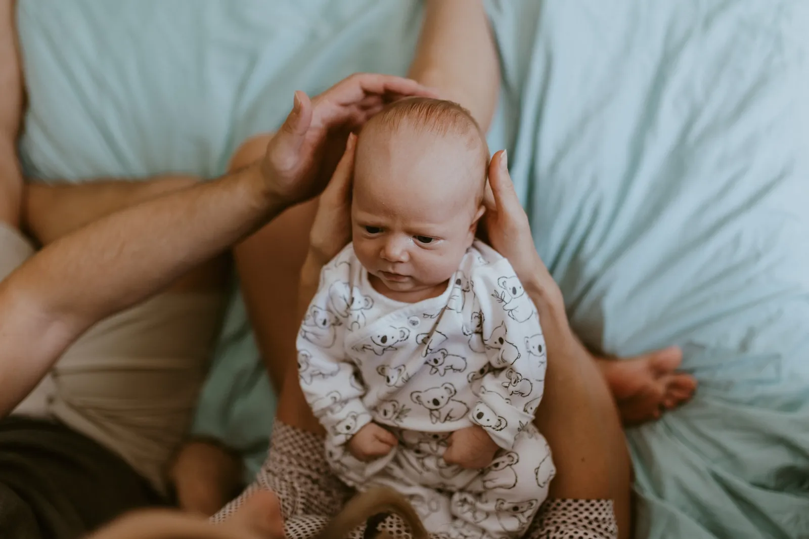 Parents' hands steadying the newborn as he sits up on the bed