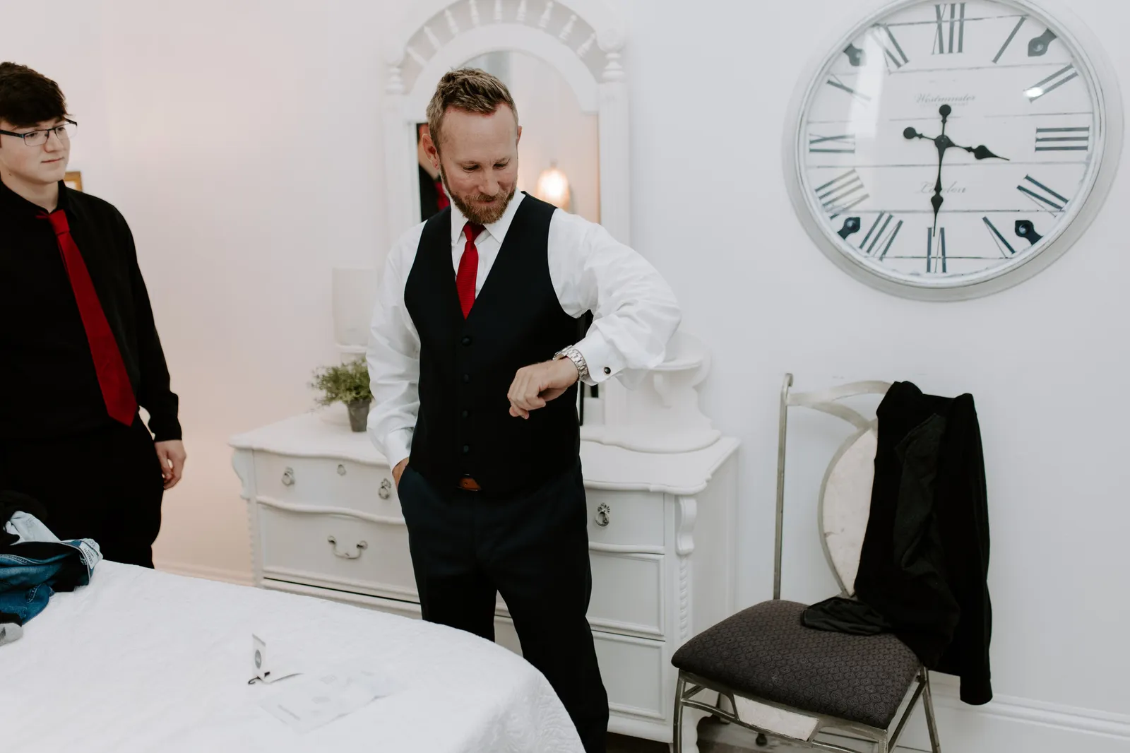 Groom in a vest and red tie checking his watch