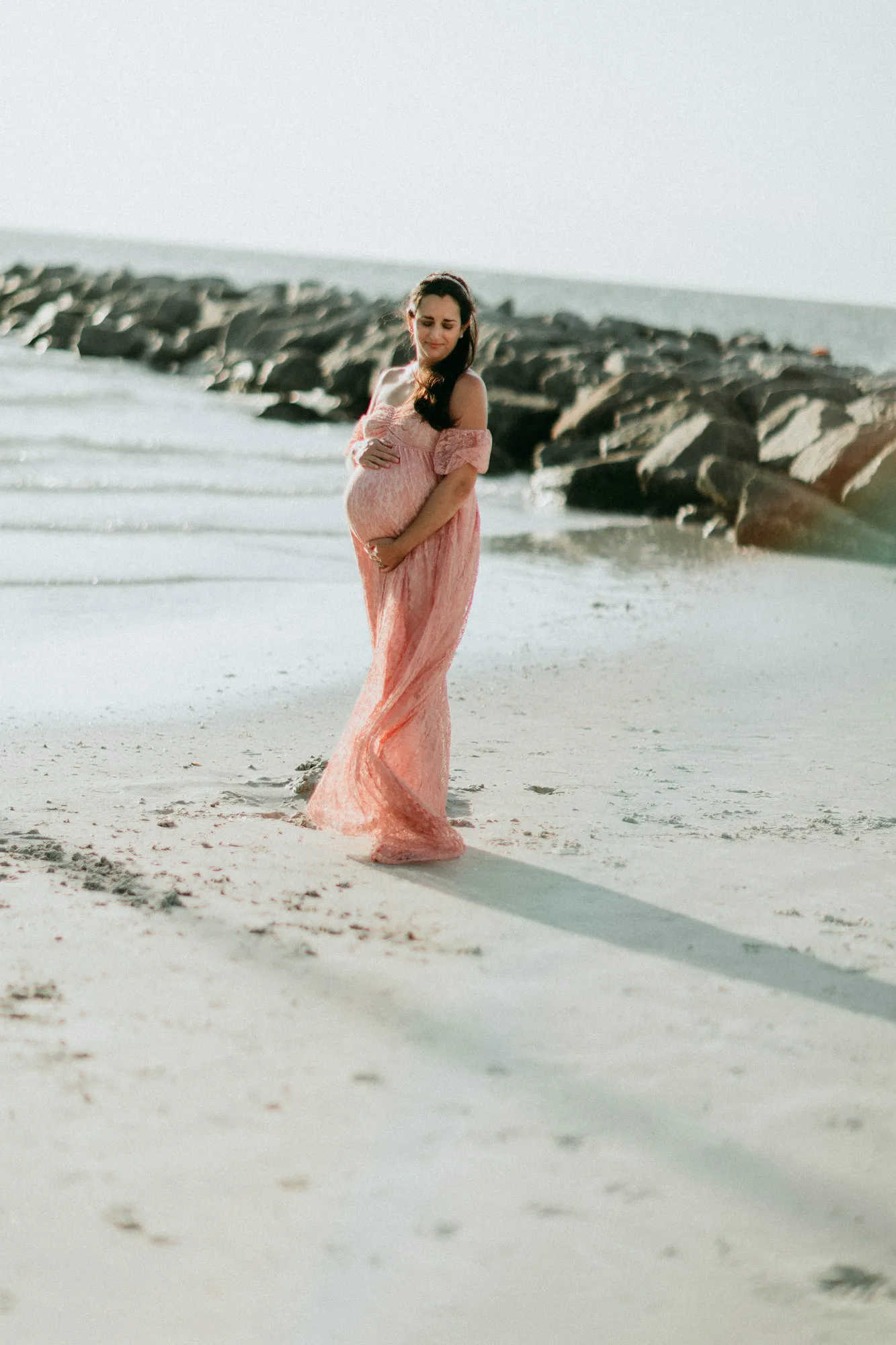Expectant mother holding her bump, facing the camera on the beach
