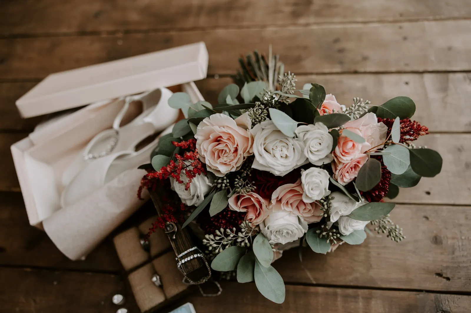 Bouquet of blush roses and red berries beside the boxed bridal shoes
