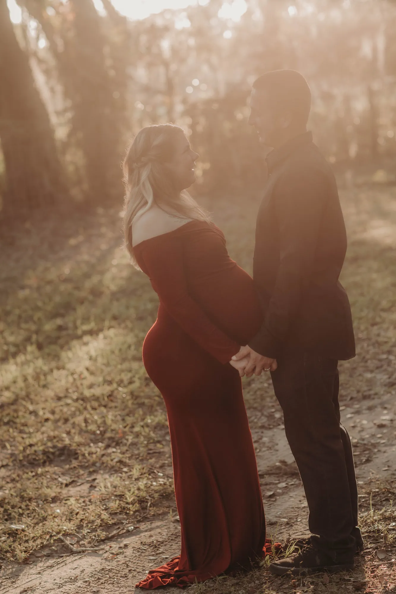 Couple standing close in hazy golden light, his hand on her bump