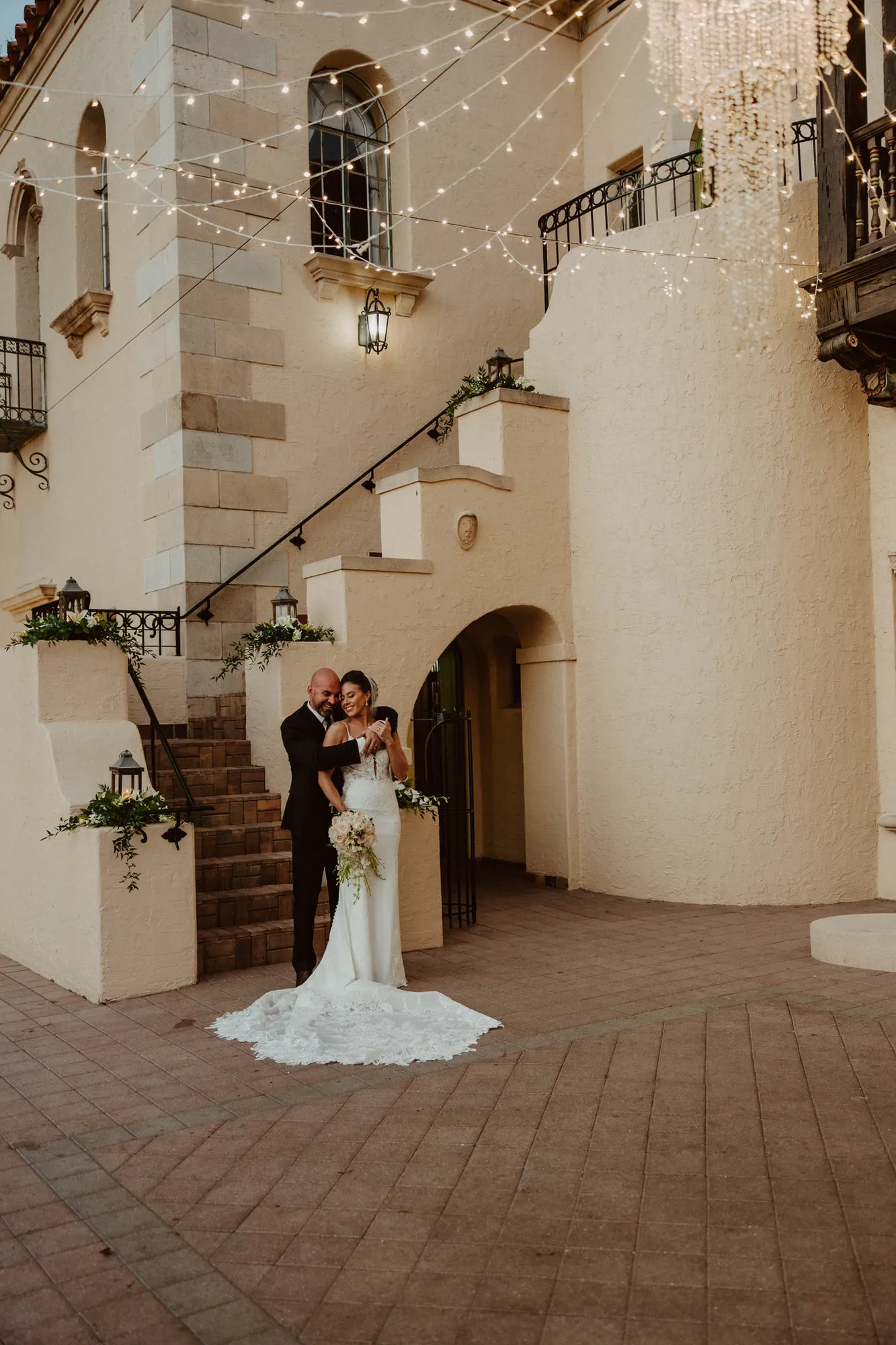 Bride and groom embracing at the foot of the Powel Crosley Estate staircase under string lights
