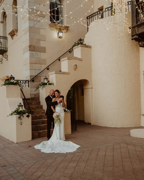 Bride and groom embracing at the foot of the Powel Crosley Estate staircase under string lights