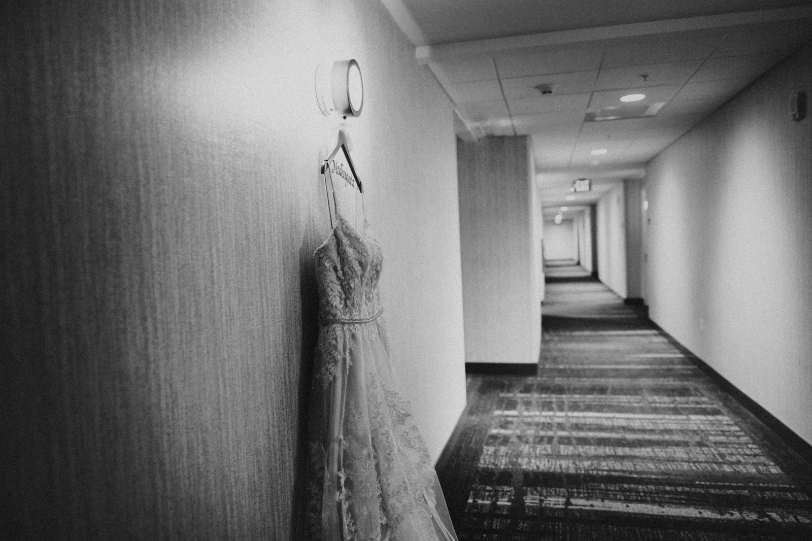 Wedding dress hanging in a hotel corridor, in black and white