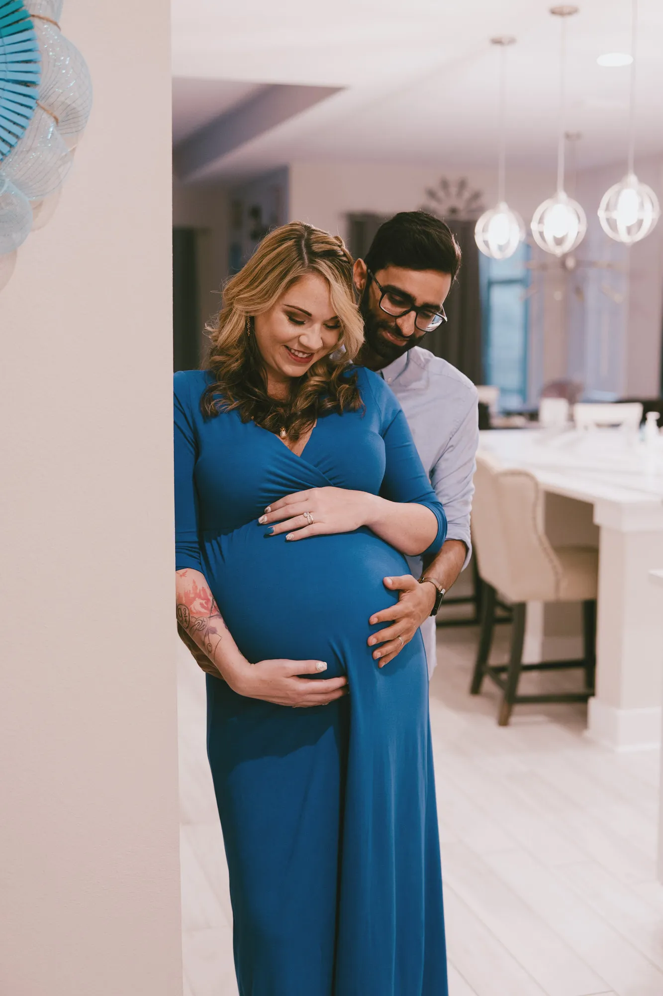 Expectant mother in the blue dress at home, her partner behind her