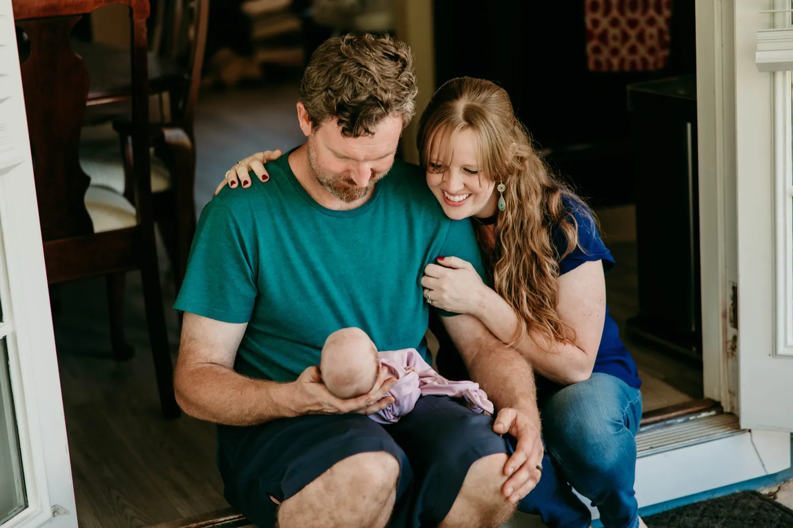 New parents sitting in their doorway holding their newborn daughter